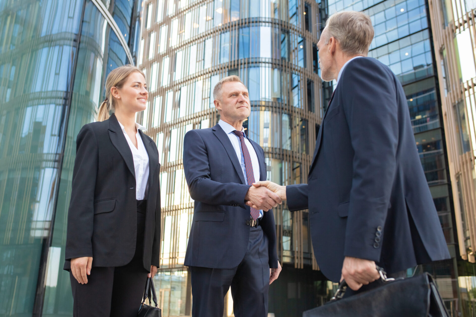 Confident business partners meeting in city, shaking hands near office building. Low angle shot. Cooperation and partnership concept